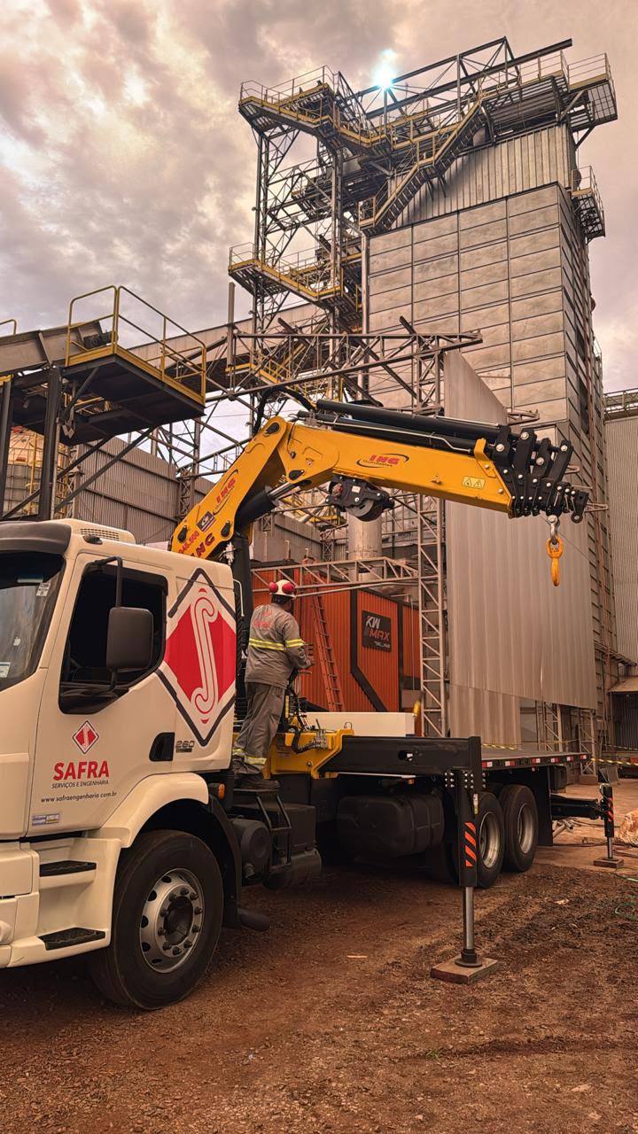 Caminhão munck içando equipamento ao lado de silo em agroindústria